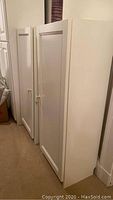 Two white storage cabinets side-by-side showing front doors and brass knob handles.