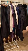 Rack of various ladies clothing including pants, tops, and a coat hung on hangers.