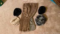Photo displaying a beige mink fur shawl alongside four fur hats in black, cream, and gray tones.
