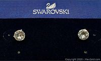 Front view of Swarovski solitaire crystal stud earrings on branded blue card showing crystal sparkle and setting detail.