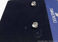 Close-up photo of the pair of Swarovski solitaire crystal stud earrings resting on a blue Swarovski branded display card.