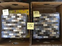 Two boxes of glass mosaic tile sheets with sand blend colors including grey, beige, brown, and white, stacked neatly.