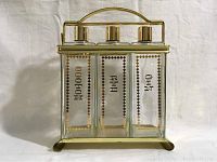 Front view of three glass decanters in gold-tone metal case showing labels and lids