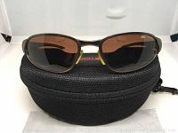 Front view of Bolle Vanadium polarized wrap sunglasses resting on black zippered case.