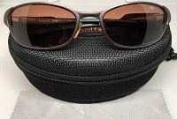 Front view of Bollé Titan 2.0 polarized sunglasses resting on a black zippered carrying case with a provided cleaning cloth underneath.