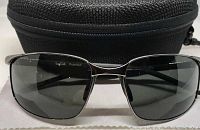 Front view of Bolle polarized sunglasses with dark lenses in front of black zippered carrying case and white cleaning cloth.
