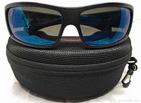 Front view of Bolle Tetra satin black sunglasses with blue polarized lenses positioned on black zippered protective case.