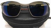 Front view of Bolle Cruise sunglasses on top of black zippered hard case showing blue GP10 frame and polarized aluminum lenses with slight scuffing visible