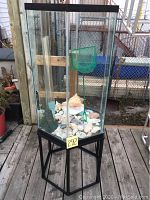 Full view of hexagonal glass aquarium tank on black metal stand with sea shells inside and green fish net hanging.