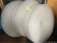 Three rolls of bubble wrap stacked vertically, clear plastic, varying widths but around 8 inches.