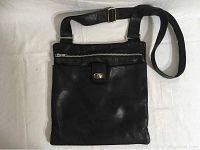 Full front view of the black leather crossbody bag showing the zippered pocket, flap pocket with silver-tone turn-lock, and adjustable strap.