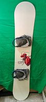 Full view of the snowboard with bindings and snowboarding shoes on top, showing white board with red ant graphic.