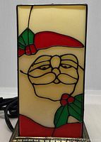 Front of the Stainglass style lamp showing Santa Claus face and mistletoe design with electrical cord coiled beside.