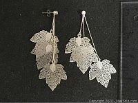 Pair of silver color metal leaf stud earrings laid flat showing the delicate layered filigree leaf design and stud backs.