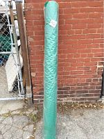 Full roll of fabric standing upright outdoors against a brick wall, wrapped in plastic with label tag number 402