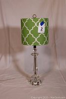 Full front view of the crystal table lamp with green and white geometric pattern shade, lamp standing on a white surface with beige backdrop.