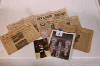 Six historic Phoenixville newspapers, a book, and the glass milk bottle arranged on a white surface, showing text and titles clearly.