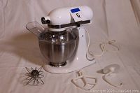Full view of KitchenAid mixer assembled with bowl and three attachments laid out on white cloth background.