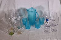 Full set displayed against white background including oversized wine glasses with colored bases, blue pitcher with lid, and 4 short blue tumblers.
