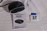 Black Jensen AM/FM clock radio with digital display, power cord, and user manual placed on white surface.