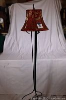Full view of the black wrought iron floor lamp with maroon and gold patterned fabric shade on a white backdrop.