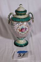 Front view of the ornate urn showing turquoise banding, gold accents, floral medallion, and two handles.