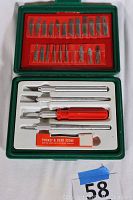 Opened green plastic case with red foam insert showing four metal knife handles, a plastic red-handled holder, and boxed pocket and desk sharpening stone along with multiple blade slots (some empty).