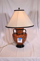 Full view of ceramic lamp showing burl wood style glaze and black base, handles, and trim, with beige lampshade trimmed in black