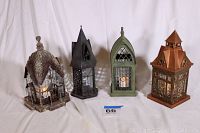Front view of all four decorative metal candle lanterns in a row, showing varied styles and colors, each approximately 11 inches tall