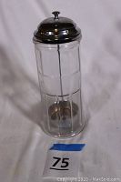 Front view of vintage glass cylindrical dispenser with metal lid and internal metal rod and base