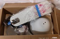 Box of new ceiling fan parts including motor assembly, fan blades wrapped in plastic, light fixture dome, and mounting hardware.