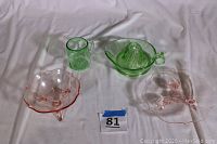 Four pieces of visible pink and green Depression glass on white fabric: mug, juicer, bowl, and footed dish.