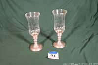 Pair of hurricane candle lamps with pewter weighted bases and clear glass etched shades shown against green background.