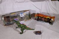 Photo shows large green remote control dinosaur toy out of box with working remote and batteries, alongside boxed 4-pack of dinosaur action figures.