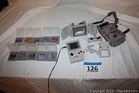 Complete lot overview showing Game Boy console, 11 game cartridges, two controllers, Hardy Boy Joyplas magnifier, carrying bag, and power adaptor on white surface.