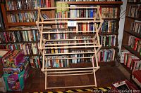 Front view of the wooden drying rack showing its multiple horizontal poles and natural wood finish, set against bookshelves.