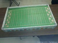 Full view of the game board showing green field with yard lines and gray border with NFL logos.