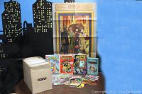 Photo of collection box containing over 120 comic books with visible example comic covers, Batman hologram stickers, and a fold-out poster propped behind them against a blue background.