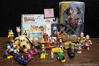 Lot showcasing a wide assortment of vintage Disney character figurines, small vehicles, books, and boxed collectibles on a table against a black background.