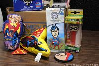 Photo showing Superman vinyl puffy suction characters, Superman playing card, Robin PEZ dispenser with Pop figure, Superman circular object with Superman head logo, all arranged in front of the DC Legion Of Collectors box