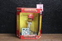 Front view of Mark McGwire bobblehead figure in original red packaging and display case, showing figure and trading card inside.