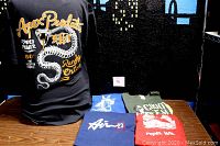 Display of 5 t-shirts including Apex Predator Randy Orton black shirt with snake graphic, Nike Air dark blue shirt, and more on table.