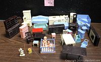 Wide assortment of dollhouse furniture and baby figures arranged on wooden surface against dark background.