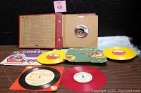 Photo showing the red album binder open with visible 45 RPM records in paper sleeves and colored red label
