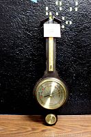 Front view of the entire instrument showing the thermometer on the wooden base against a black background