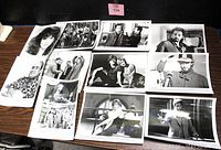 Photo of assorted vintage 8x10 glossy black and white studio film photos spread out on table showing different actors in various film scenes and studio portraits.