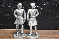 Front view of two pewter figurines depicting U.S. Civil War generals William T Sherman and George G Meade on flat wooden surface with black background.