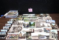 Wide view of numerous vintage postcards and photographs laid out on a table showing various scenes including architecture, landscapes, and people.