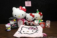 Photo showing entire Hello Kitty lot including alarm clock, two plush toys, small figures, eraser, tin candy box, phone holder, and pajama top all arranged on surface against black background.