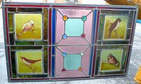 Front view of stained glass panel held outdoors showing full design and hanging chain.